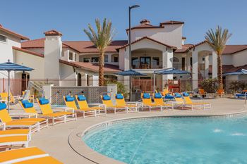 A pool with chairs and umbrellas in front of a house at The Villas at Ellis Manor, Fresno, California